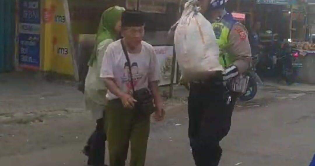 Anggota Unit Polsek Sukaraja Menolong mengangkat barang jualan kakek Yang Tampak Kesulitan Membawa Sebuah Karung