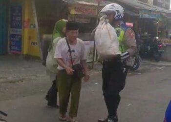 Anggota Unit Polsek Sukaraja Menolong mengangkat barang jualan kakek Yang Tampak Kesulitan Membawa Sebuah Karung
